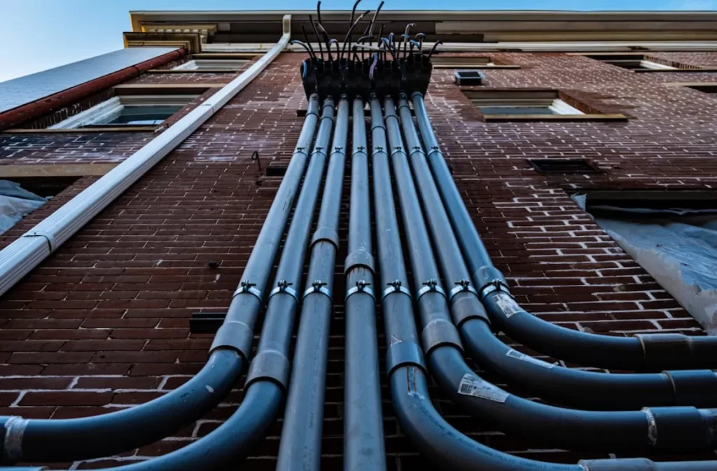 Steel pipelines aligned vertically against a brick wall.