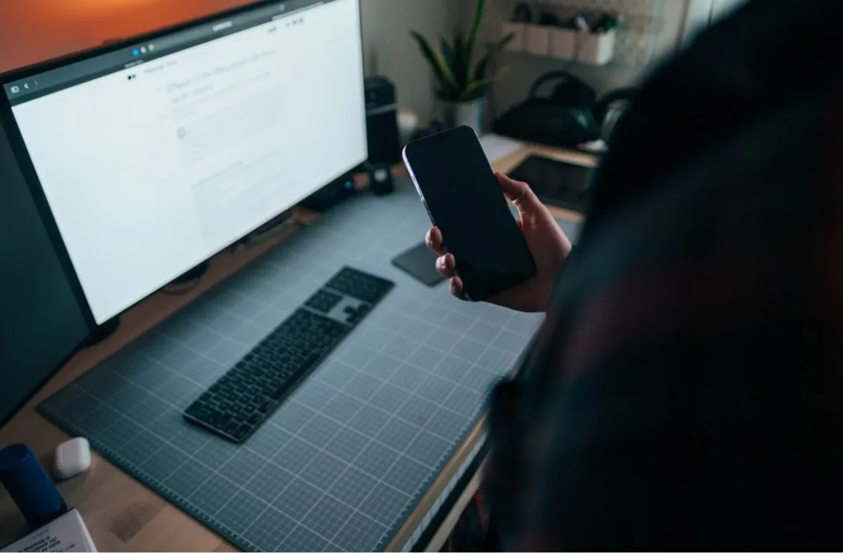 Hand holding phone in front of a computer screen.