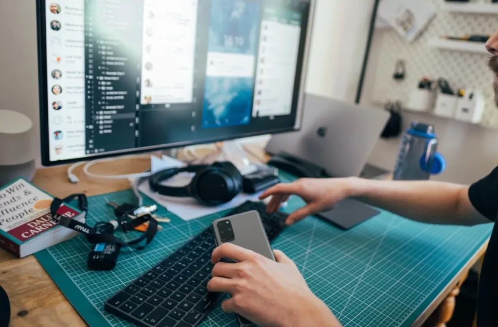 Person working on a computer with phone in hand.