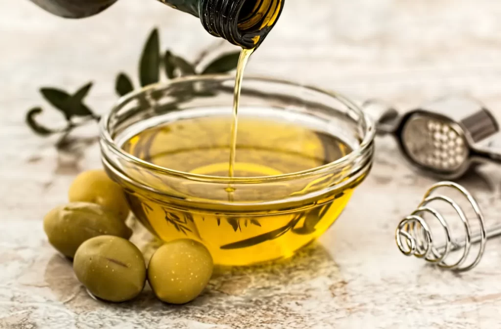 Golden oil poured into a bowl, olives nearby.
